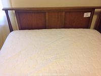Front view of mattress on wooden headboard and footboard, showing quilted mattress cover and panel design on wood.