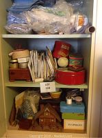 Shelves filled with sewing accessories including tins, yarn, fabric in plastic bags, and a wooden miniature house-shaped sewing box.