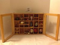 Full front view of the wooden and glass shadow box with doors open, showing all compartments filled with assorted figurines and decorative eggs.