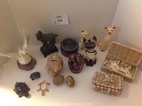 View of the entire assortment including cat figurines, coin banks, small carved animals, eggs, and woven baskets with shells.