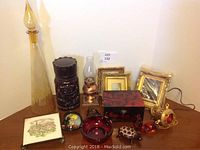 Photo of full lot items including tall amber bottle, musical jewelry box, frames, lantern, and small figurines on wooden surface