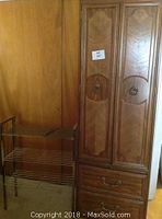 Pressed wood entertainment cabinet with paneled doors closed next to vintage metal wire rack with three wire shelves.