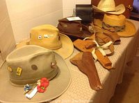 Image showing a variety of hats including beige, yellow straw, brown leather cowboy hat, black bag, and leather gun holsters.