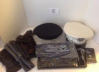 Photo showing white men's military peaked cap with insignia, black beret, several pairs of men's gloves in brown and gray, black bow tie in box, black cummerbund in original packaging, and a small black booklet.