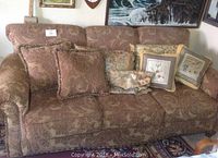 Full front view of three-seat upholstered sofa with paisley pattern and multiple decorative pillows resting on seat cushions.