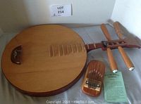 Front view of the Asian stringed instrument with natural wood finish and four tuning pegs beside the Mountain Melody thumb piano and info card.