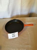 Top view of a 9 inch enameled cast iron skillet with orange handle and black interior surface.