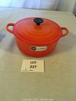 Le Creuset orange enameled cast iron Dutch oven with lid on, showing front and handles.