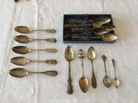 15 spoons displayed on table, group arrangement includes spoons in box, arranged in rows and decorative spoons at bottom