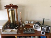 Top view of bookcase with an assortment of small decorative and mechanical items including clocks, gauges, and miniature piano model.