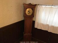 Full view of the tall oak case style clock showing its height and wood structure.