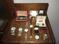 Full view of lot on wooden bench with watches, cufflinks, rings, knife, and compass