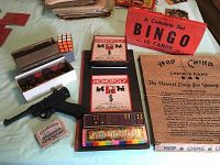 Overhead image showing assortment of vintage board games and toy pistol on a table including Monopoly, Bingo cards, Hop Ching Checker Game, Colour Dominoes, Rubik's Cube, Steamships playing cards, and a toy handgun.