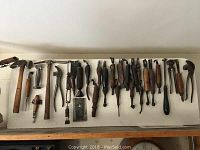 Display board mounted with assortment of wooden-handled cobbler tools including hammers, pliers, awls and scrapers