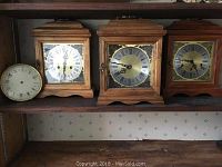 Three wooden mantel clocks on shelf, front view showing faces, one clock face missing