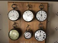 Front view of all six pocket watches displayed on wooden board