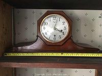 Full front view of the wooden mantel clock showing overall design and approximate 21 inch width with measuring tape.