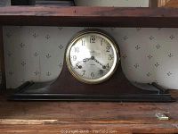 Full front view of the Ingraham mantel clock showing the wooden body on a shelf.