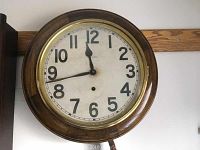 Front view of New Haven antique wall clock showing round wooden frame, glass cover, white face with black numerals and black hour and minute hands.