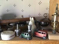 Shelf with two die-cast Tootsie Toy cars, ceramic dog figurine, rope coil, enamel trinket box and various small metal parts