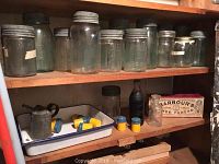 Wooden shelf with multiple antique glass Mason jars of varying sizes and embossed brands