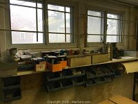 White-top shelving under window with small boxes and blue bins filled with screws, nails, bolts.