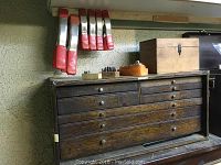 Oak multi-drawer tool chest topped with small wooden box and red-handled clamps