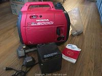 Front view of red Honda EU2000i inverter generator with manual on hardwood floor