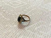 Side angle view of a gold ring with black onyx stone and diamond detail, laid on textured light fabric surface.