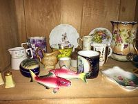 Assorted china pieces on wooden shelf including pitchers, plates, moustache cup, condiment set, and small bowls all with floral and colorful patterns.
