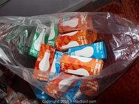 Plastic bag containing assorted unopened boxes of incandescent light bulbs in orange, blue, and green packaging on a red chair.
