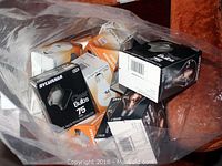 Multiple unopened Sylvania brand 75 watt incandescent light bulbs in black and orange/white cardboard boxes inside a clear plastic bag.