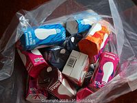 Photo showing multiple Sylvania incandescent light bulbs in various packaging colors including blue, pink, and orange inside a transparent bag.