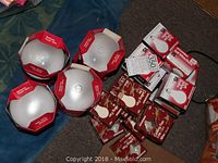 Four white reflector flood lights in red and white boxes next to various boxes of light bulbs in red and brown packaging arranged on carpet and blanket