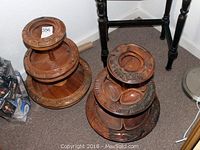 Two carved three-tier wooden Lazy Susans side-by-side on floor next to furniture