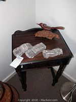 Full view of wood side table with three clear glass car figurines and carved wooden bird on top, showing wear and scratches on table surface