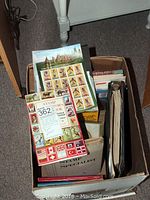 Overhead view of a box filled with various stamp collecting books and sheets with an old India-themed sheet visible
