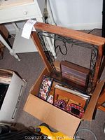 Box filled with assorted picture frames and small wall shelf shown from top angle. Included large wooden frames, smaller decorated frames, and various sizes.