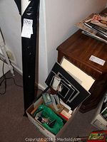 Photo showing a box containing matting materials, small tools, bubble wrap, and a black wrapped item standing next to a wooden cabinet
