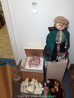 Overview of porcelain figurines including doll and boxed flower arrangement