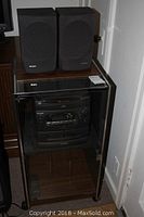 Sony stereo system including disc player, radio, housed in cabinet with two Sharp speakers on top.