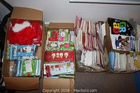 Four boxes of assorted greeting cards arranged side by side, showing diverse holiday card stacks and Santa hats on top.