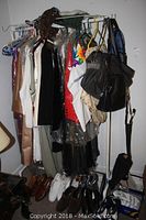 Clothing rack holding assorted women's vintage clothing, handbags, and shoes arranged below