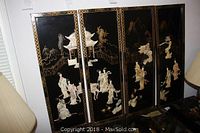 Four black lacquer panels with gilt and mother of pearl decorative Chinoiserie scenes leaning against a wall.