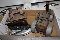 Box containing the vintage iron, toy sewing machine, and toy tractor together showing scale and condition.
