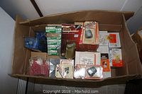 Top view of packed box containing various electrical supplies including lamp holders in blister packs and other small packages.