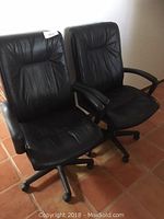 Two black office chairs side by side showing padded seats and backrests, armrests, and castored bases