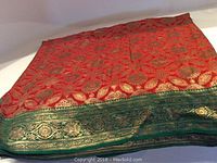 Folded red and green silk brocade fabric with gold floral and leaf motifs visible on the front side