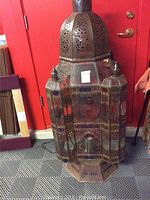 Full front view of aged bronze iron Moroccan lantern with glass panels and perforated dome top.