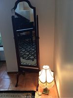 Full view of the tall standing mirror with wooden frame and the lamp on the floor beside it.